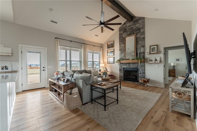 living room with ceiling fan, high vaulted ceiling, a fireplace, beamed ceiling, and light wood-type flooring