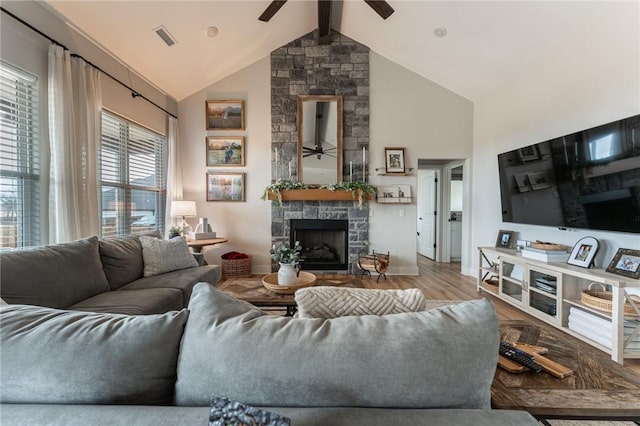 living room featuring beam ceiling, a stone fireplace, hardwood / wood-style floors, and ceiling fan