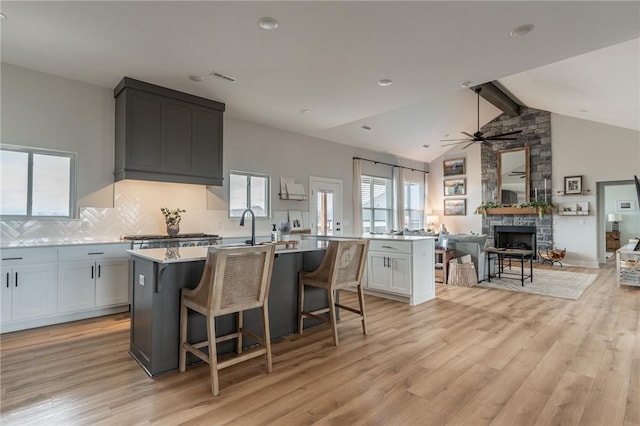 kitchen with a fireplace, white cabinetry, a breakfast bar area, a kitchen island with sink, and light hardwood / wood-style floors