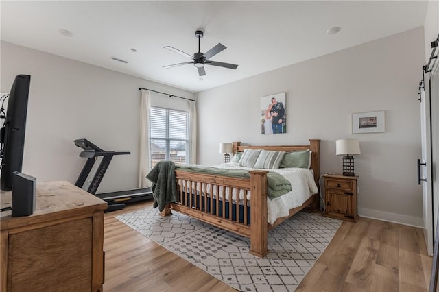 bedroom featuring a barn door, ceiling fan, and light hardwood / wood-style flooring