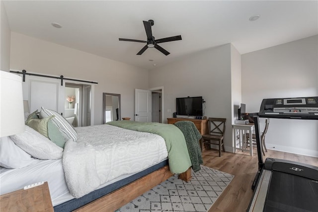 bedroom with ceiling fan, wood-type flooring, and a barn door