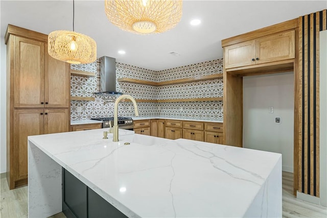 kitchen featuring wall chimney exhaust hood, stainless steel gas stove, light wood-type flooring, pendant lighting, and light stone countertops