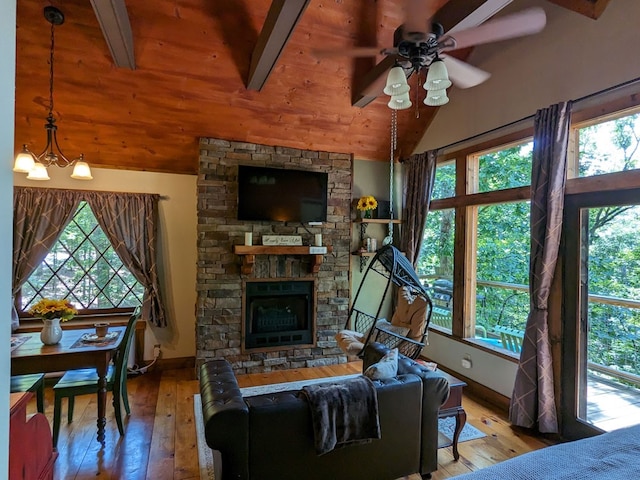 living room featuring a stone fireplace, ceiling fan with notable chandelier, lofted ceiling with beams, wood-type flooring, and wooden ceiling