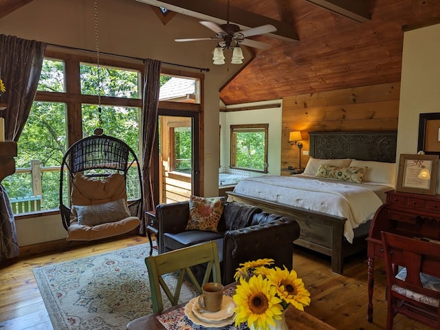 bedroom featuring lofted ceiling with beams, wood walls, multiple windows, and light hardwood / wood-style flooring