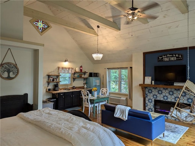 bedroom featuring a chandelier, fridge, beam ceiling, a tiled fireplace, and hardwood / wood-style floors