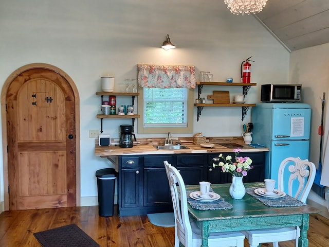 kitchen featuring vaulted ceiling, wood counters, refrigerator, sink, and hardwood / wood-style flooring