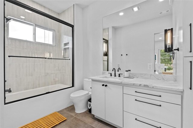 full bathroom featuring bath / shower combo with glass door, vanity, tile patterned floors, and toilet