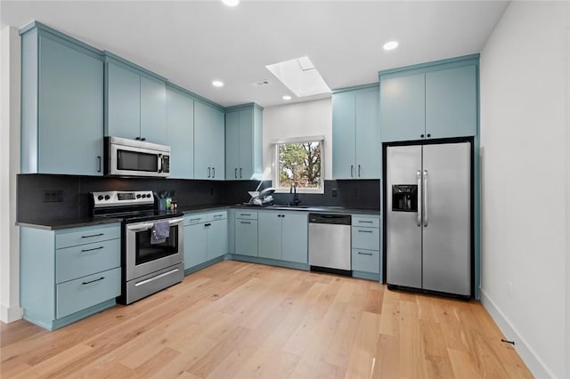 kitchen featuring sink, backsplash, a skylight, stainless steel appliances, and blue cabinets