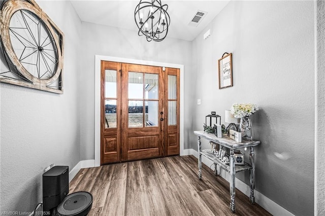 foyer entrance featuring visible vents, a notable chandelier, baseboards, and wood finished floors