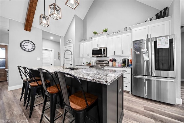 kitchen with a breakfast bar, appliances with stainless steel finishes, white cabinets, a sink, and an island with sink