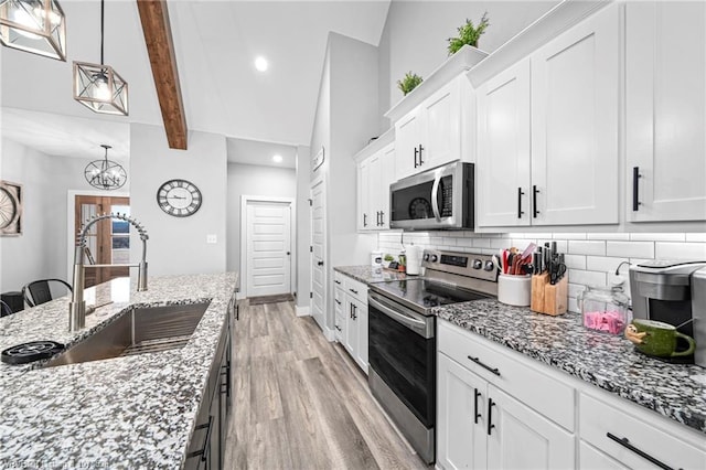 kitchen with appliances with stainless steel finishes, a sink, decorative light fixtures, and white cabinetry