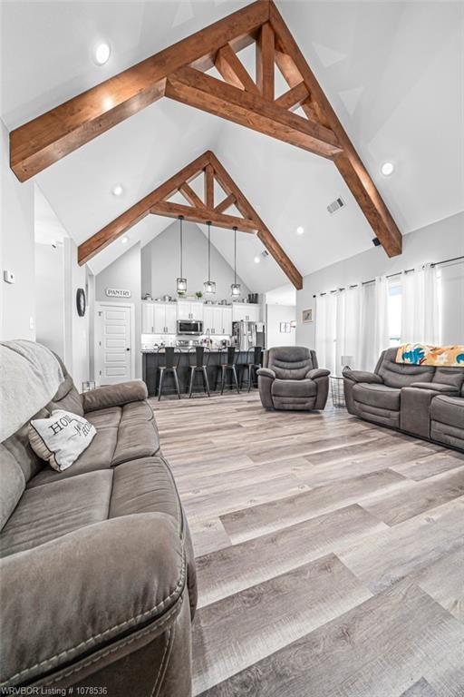 living room with high vaulted ceiling, light wood-style flooring, beam ceiling, and visible vents