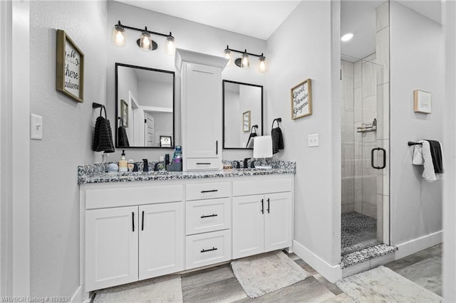 full bathroom featuring double vanity, a sink, a shower stall, wood finished floors, and baseboards