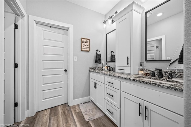 full bathroom with double vanity, wood finished floors, a sink, and baseboards