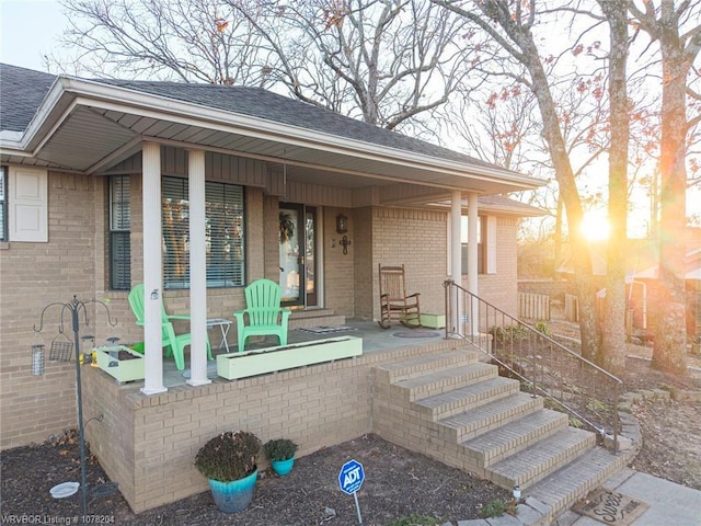 property entrance featuring a shingled roof, a porch, and brick siding