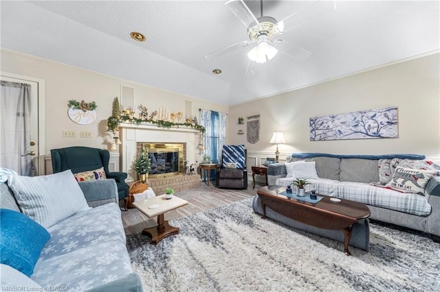 living area with a brick fireplace, ceiling fan, wood finished floors, and a wainscoted wall