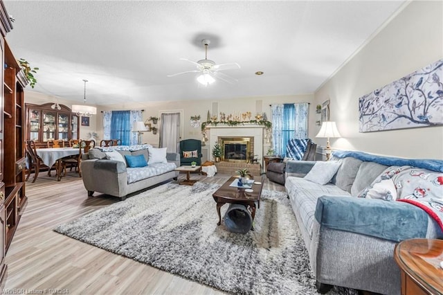 living area featuring light wood-style floors, a fireplace, ornamental molding, and ceiling fan with notable chandelier