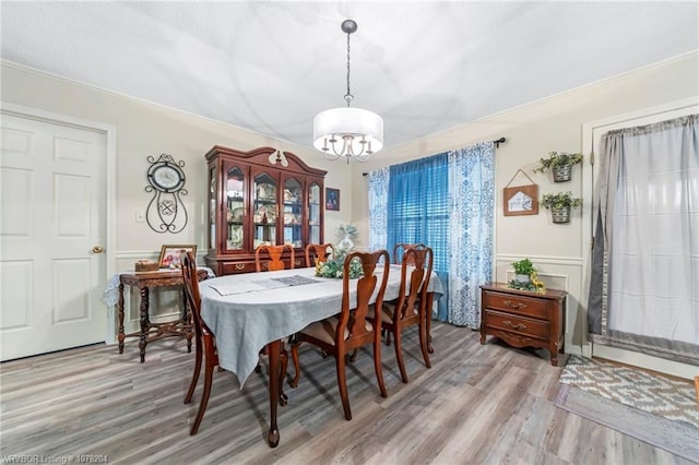 dining area featuring light wood-type flooring, a chandelier, a decorative wall, and wainscoting