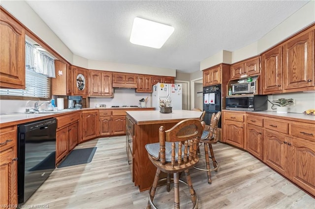 kitchen featuring a center island, light wood finished floors, light countertops, brown cabinetry, and black appliances