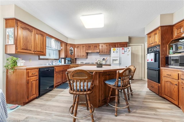 kitchen with a kitchen island, a kitchen breakfast bar, light countertops, black appliances, and brown cabinetry