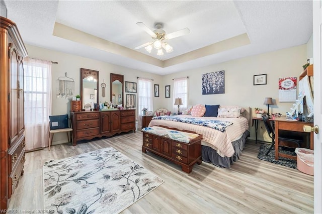 bedroom featuring light wood-style floors, a raised ceiling, and multiple windows