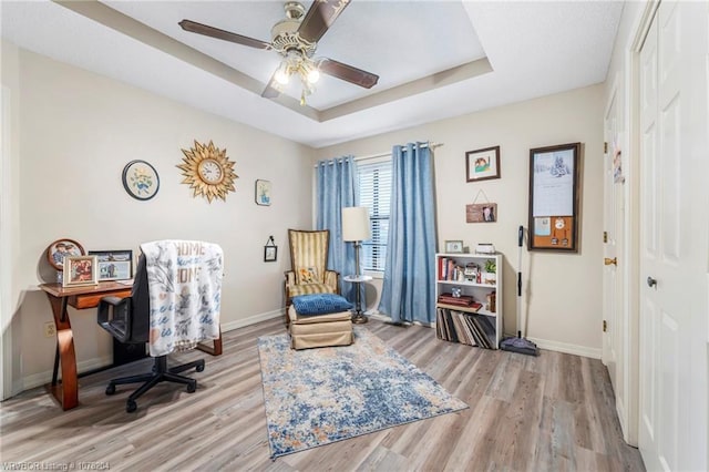 office space with light wood-style floors, a tray ceiling, and baseboards