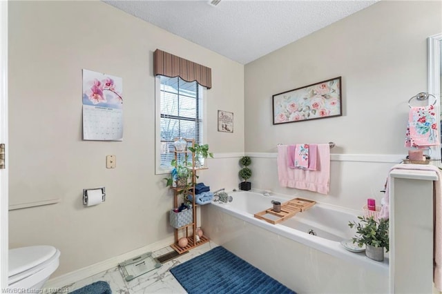 bathroom featuring a textured ceiling, a garden tub, toilet, baseboards, and marble finish floor