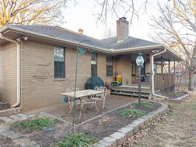 rear view of house featuring roof with shingles, a chimney, a deck, and brick siding