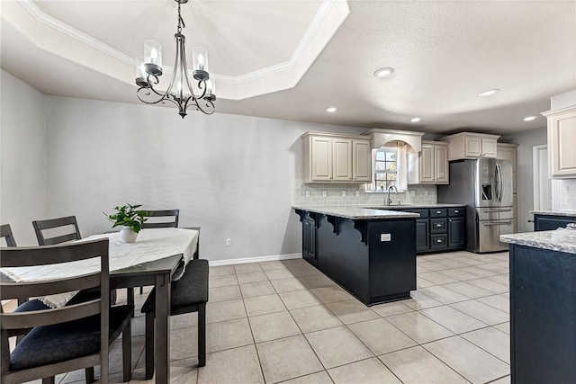 kitchen with pendant lighting, stainless steel refrigerator with ice dispenser, light stone counters, a kitchen bar, and a raised ceiling