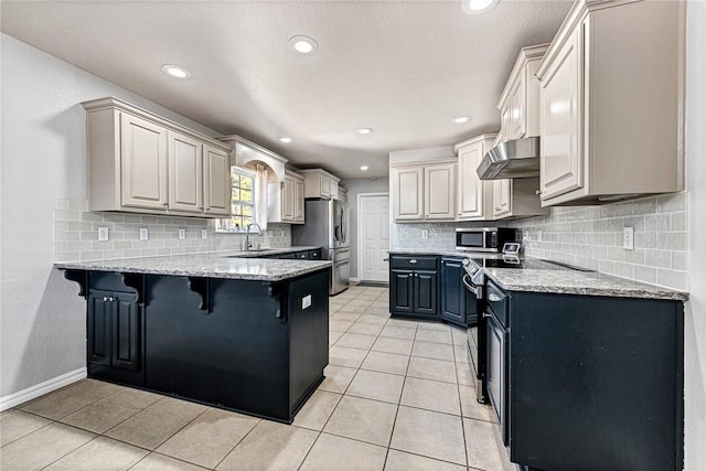 kitchen with light tile patterned flooring, appliances with stainless steel finishes, a breakfast bar area, and wall chimney exhaust hood