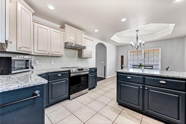 kitchen featuring light tile patterned flooring, appliances with stainless steel finishes, decorative backsplash, a raised ceiling, and light stone countertops