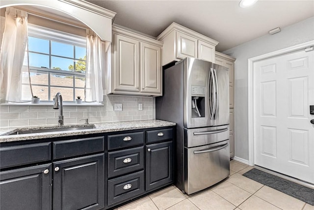 kitchen featuring sink, stainless steel fridge, backsplash, light tile patterned floors, and light stone counters