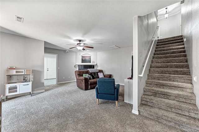 living room with a textured ceiling, carpet floors, and ceiling fan