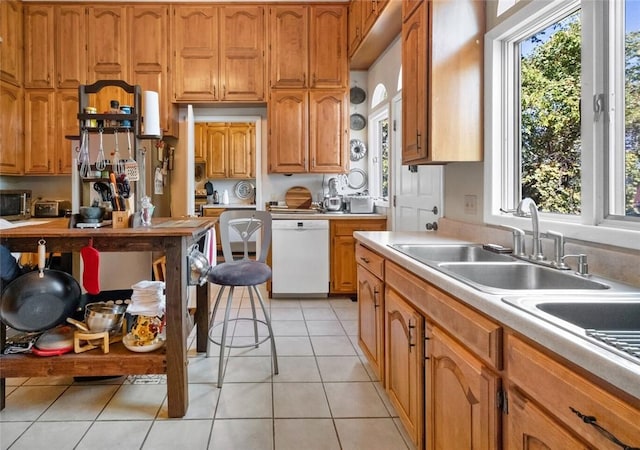 kitchen featuring dishwasher, sink, light tile patterned floors, and a kitchen breakfast bar