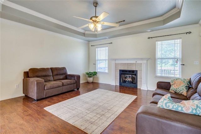 living room featuring a fireplace, a tray ceiling, dark wood-type flooring, and ceiling fan