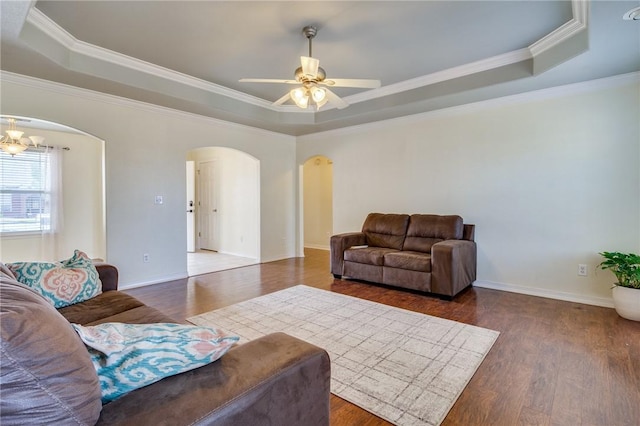 living room with a raised ceiling, ornamental molding, dark hardwood / wood-style floors, and ceiling fan with notable chandelier