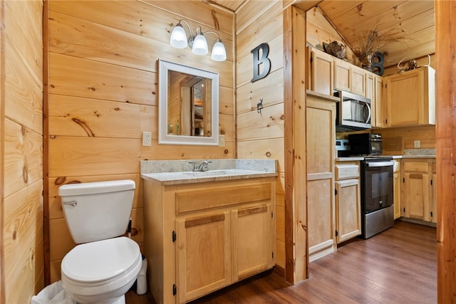 bathroom featuring hardwood / wood-style floors, vanity, vaulted ceiling, toilet, and wood walls