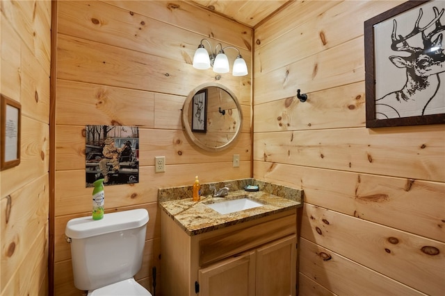 bathroom with toilet, vanity, and wooden walls