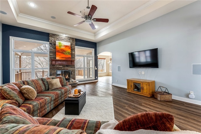 living room featuring a stone fireplace, ornamental molding, dark hardwood / wood-style floors, and a raised ceiling