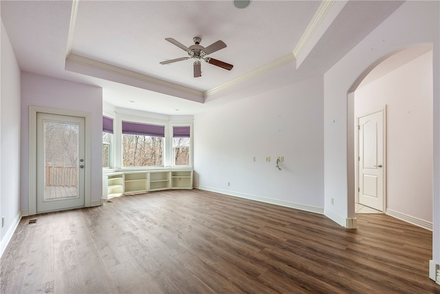 unfurnished living room with ornamental molding, dark wood-type flooring, ceiling fan, and a tray ceiling