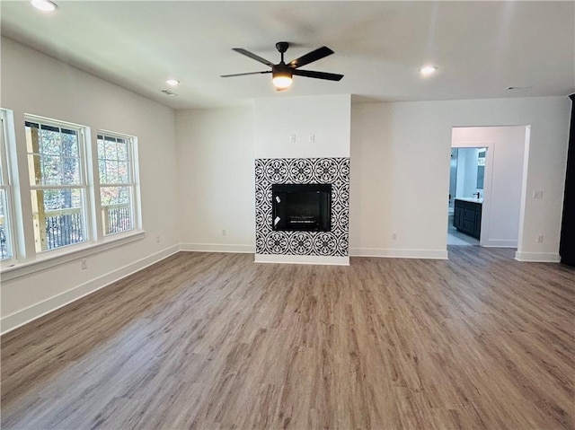 unfurnished living room featuring a tile fireplace, ceiling fan, and light wood-type flooring