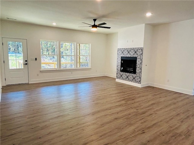 unfurnished living room with a tiled fireplace, dark wood-type flooring, and ceiling fan