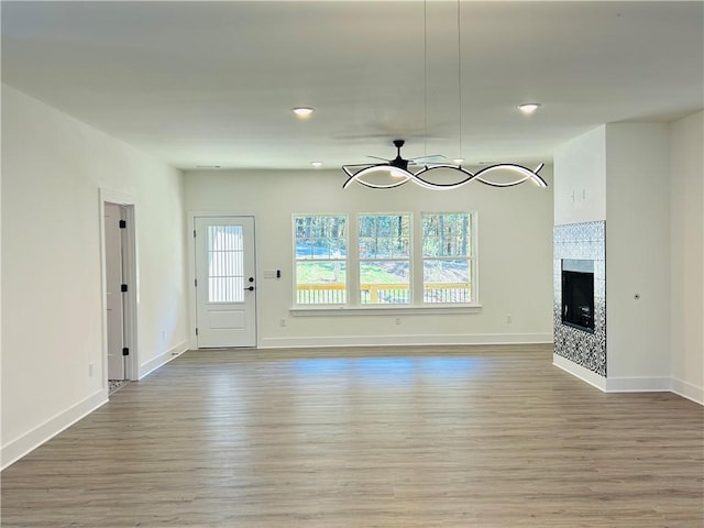 unfurnished living room with a tile fireplace, wood-type flooring, and ceiling fan