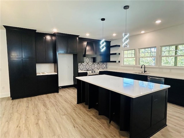 kitchen featuring pendant lighting, tasteful backsplash, a center island, wall chimney range hood, and light hardwood / wood-style flooring