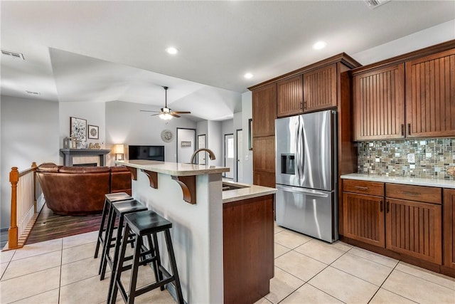 kitchen featuring sink, light tile patterned floors, stainless steel fridge, a kitchen breakfast bar, and an island with sink