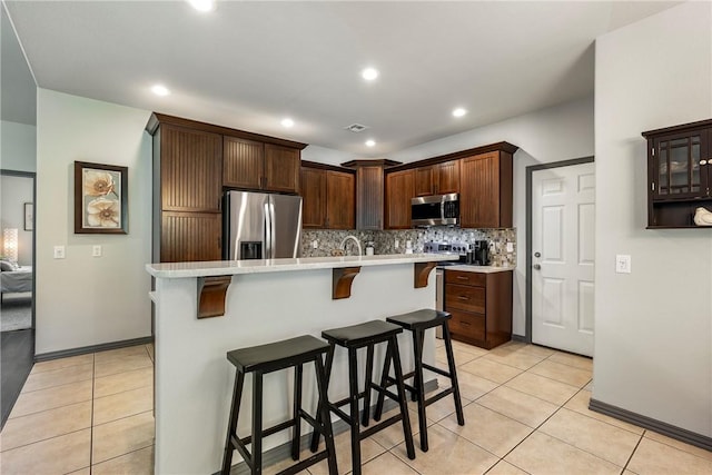 kitchen with light tile patterned flooring, appliances with stainless steel finishes, a kitchen island with sink, and a kitchen breakfast bar