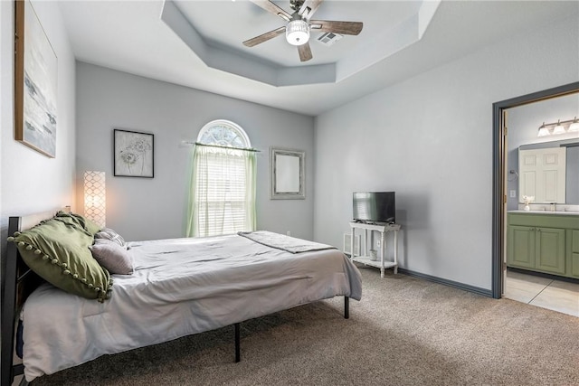 bedroom featuring ensuite bathroom, sink, light colored carpet, a raised ceiling, and ceiling fan