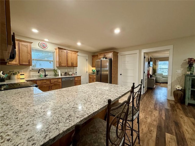 kitchen with a kitchen bar, sink, light stone counters, dark hardwood / wood-style floors, and stainless steel appliances