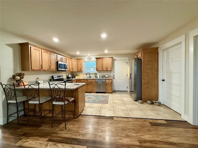 kitchen with a breakfast bar, light hardwood / wood-style floors, kitchen peninsula, stainless steel appliances, and light stone countertops