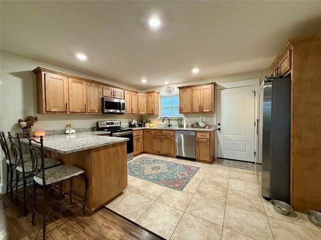 kitchen with a kitchen bar, sink, light tile patterned floors, kitchen peninsula, and stainless steel appliances